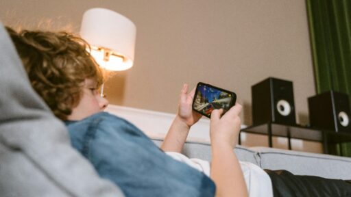 Teen lying on a sofa playing video game with speakers in background