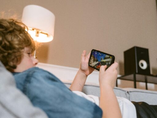 Teen lying on a sofa playing video game with speakers in background