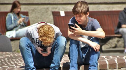 Two teenagers seated outside, using their smartphones