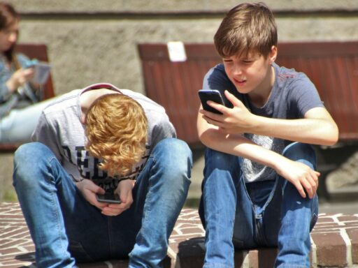 Two teenagers seated outside, using their smartphones