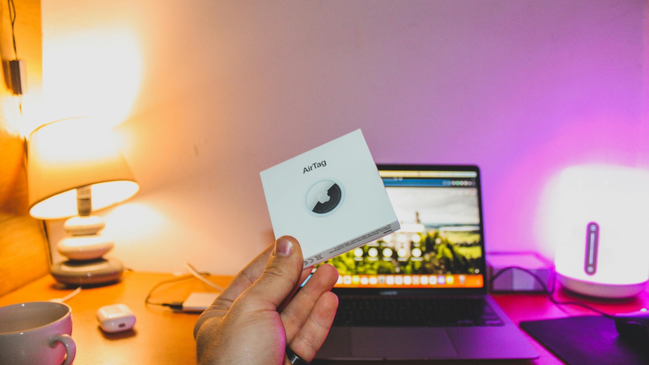 Hand holding airtag box in front of laptop